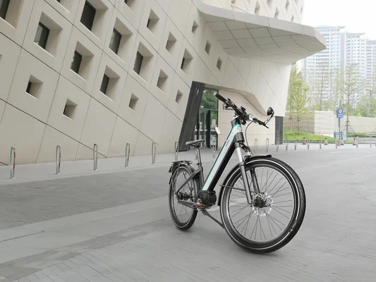 Vélo électrique blanc et noir devant un immeuble à façade perforée, vu en contre-plongée.
