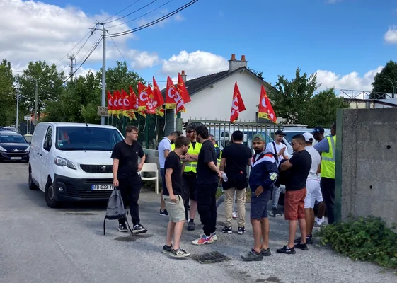 Manifestation de livreurs devant un entrepôt, avec des drapeaux CGT et une camionnette blanche.