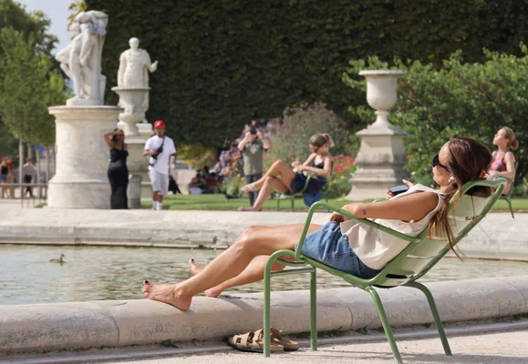 Une Parisienne profitant d'un brumisateur et d'une fontaine dans un parc pour se rafraîchir lors de la canicule.