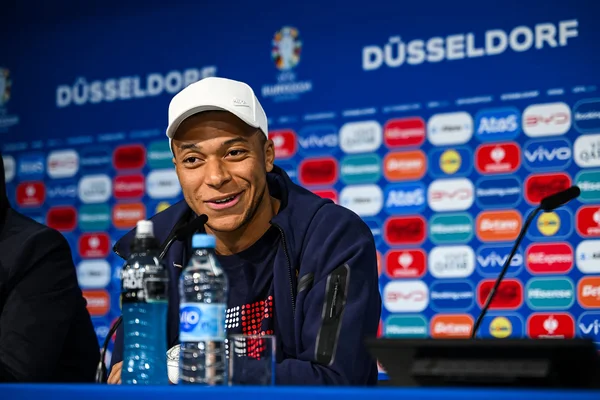 Kylian Mbappé en conférence de presse à Düsseldorf, souriant devant les micros.