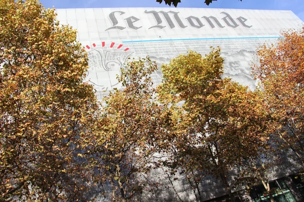 Siège du journal Le Monde à Paris, grande fresque représentant la une du journal, partiellement cachée par des arbres d'automne