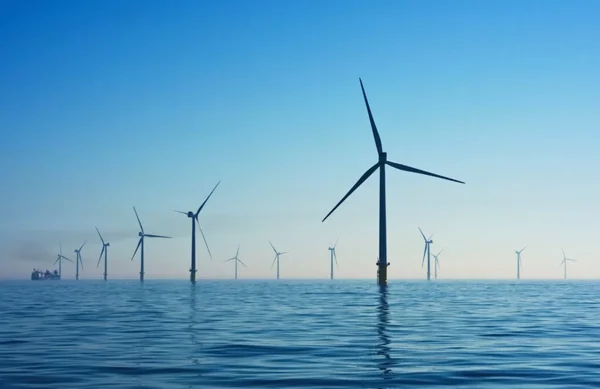 Éoliennes en mer par temps calme, avec un navire de service en arrière-plan.