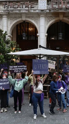 Des militantes féministes devant l'entrée du théâtre Édouard VII, avec bandeaux rouges et pancartes.