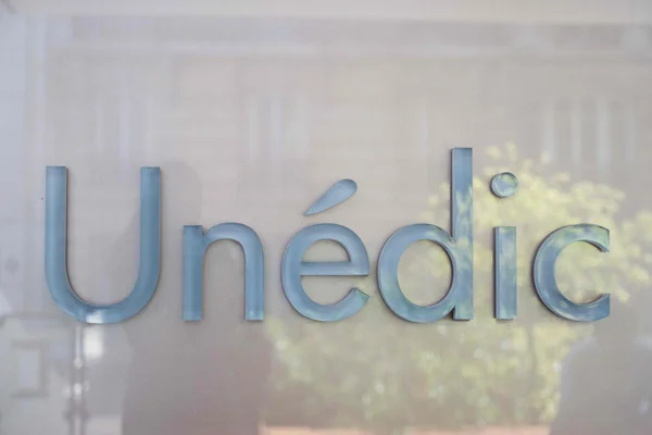 Logo d'Unédic en lettres métalliques bleues sur une façade vitrée.