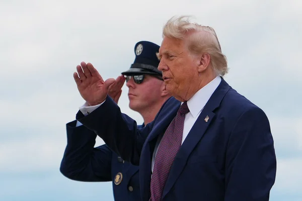 Donald Trump, la main levée en signe de salut, devant un officier en uniforme.
