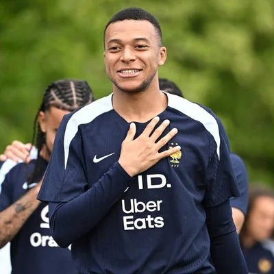 Kylian Mbappé en veste bleue de la FFF, le visage mouillé.