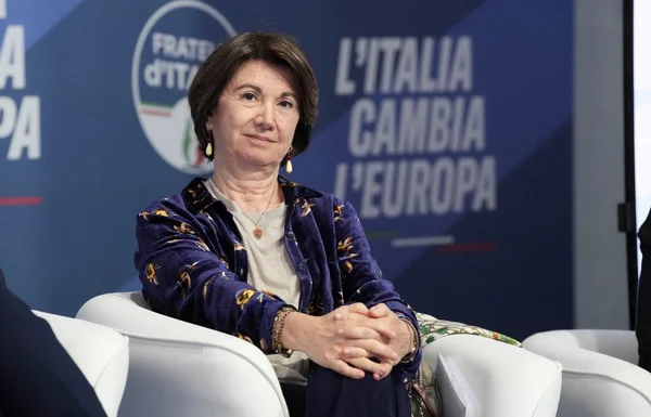 Eugenia Roccella assise dans un fauteuil blanc avec un slogan politique en arrière-plan.