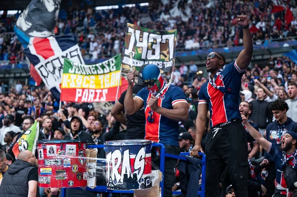 Supporters parisiens en plein chant, dont un tambourineur, au stade.
