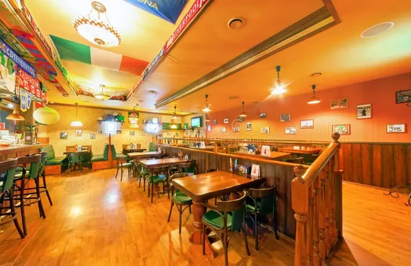 Intérieur d'un pub sportif à Boston, avec banquettes vertes et drapeaux internationaux.