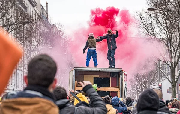 Deux manifestants sur un camion, main dans la main, dans une fumée rouge lors d'un rassemblement de teufeurs.