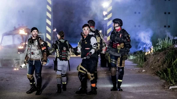 Scène post-apocalyptique de District Z avec des figurants et un véhicule en feu.