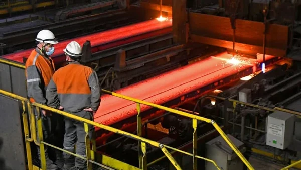 Ouvriers sidérurgistes surveillant des brames d'acier chauffées à blanc dans une usine.