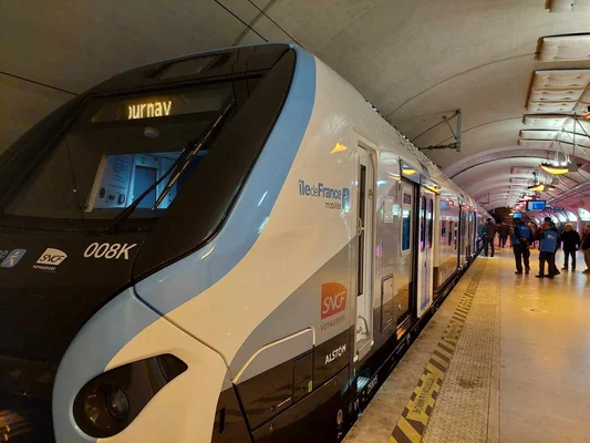 Rame de RER E à quai dans une station souterraine, avec des passagers et des agents.