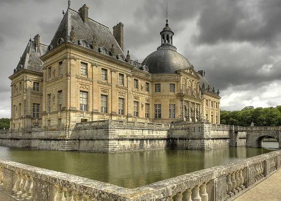 Le château de Vaux-le-Vicomte, vu depuis ses douves, sous un ciel nuageux.
