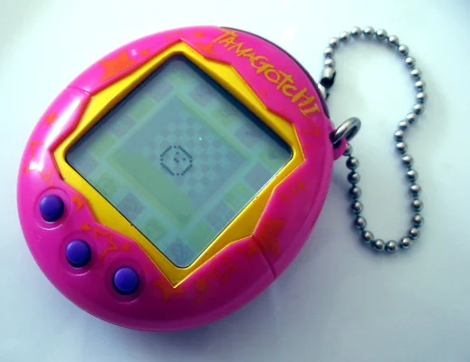 Un Tamagotchi rose et jaune avec sa chaîne à boules, posé sur fond blanc.