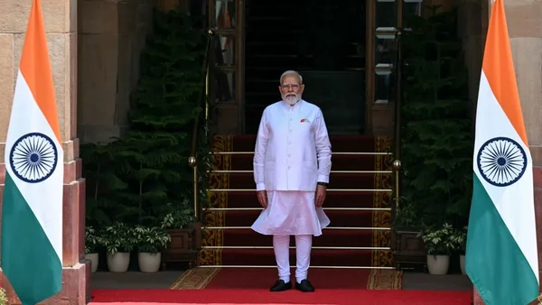 Le fondateur du Parti des cafards, vêtu d'un kurta blanc, debout sur un tapis rouge entre deux drapeaux indiens