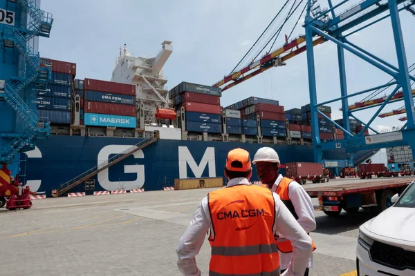 Le CMA CGM Notre-Dame, plus grand porte-conteneurs français, à quai au Havre, avec des agents portuaires au premier plan.