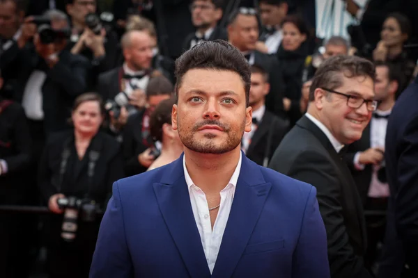Kev Adams sur un tapis rouge, entouré de photographes.