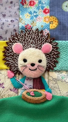Hérisson en feutrine fait main, avec tambour à broder, sur fond de patchwork coloré.