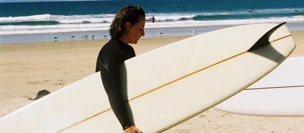 Elisa Routa sur une plage, tenant une planche de surf après une session dans l'océan.