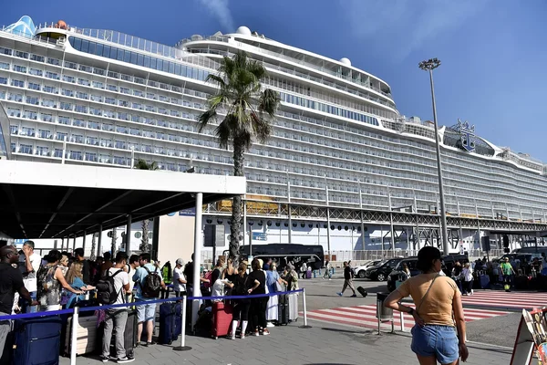 Passagers de croisière en attente avec leurs bagages devant un paquebot au port de Barcelone.