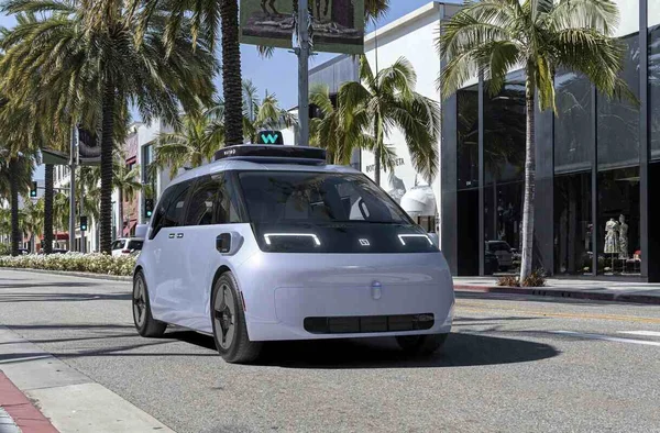 Véhicule autonome Waymo (Chrysler Pacifica) circulant dans une rue ensoleillée.