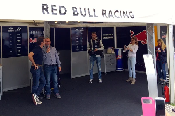 Geri Halliwell-Horner aux côtés de Christian Horner et Johnny Herbert dans un stand Red Bull Racing lors d'un événement promotionnel.