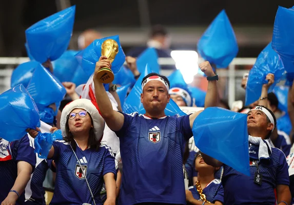 Des supporters japonais célèbrent dans le stade après un match de la Coupe du monde, arborant fièrement leur drapeau.