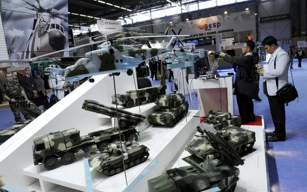 Vue générale du salon Eurosatory 2024, avec des maquettes de véhicules militaires et d'hélicoptères exposées.
