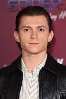 Tom Holland en veste de cuir, devant un fond Spider-Man.