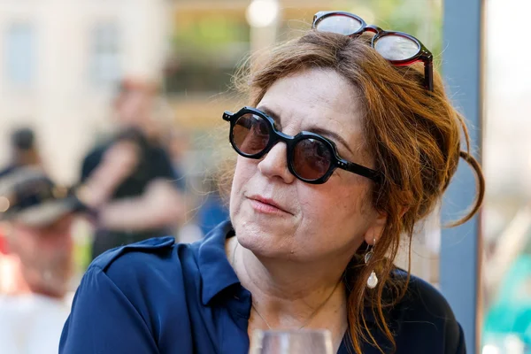 Agnès Jaoui en plan rapproché, portant des lunettes de soleil et une chemise bleue.