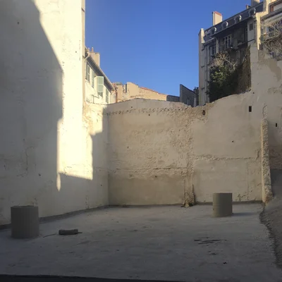 Cour ou chantier en plein air dans un quartier marseillais, avec plots de béton et immeubles environnants.