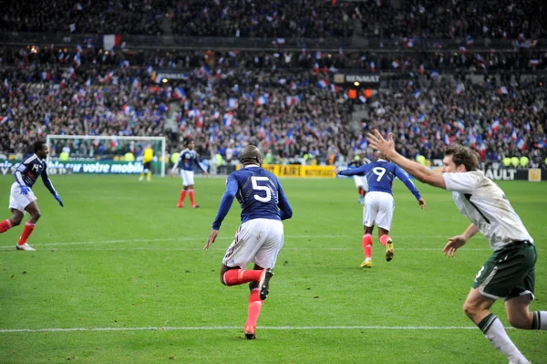 Scène de match au Stade de France : William Gallas célèbre son but avec ses coéquipiers, tandis que Kevin Kilbane réclame une faute de main.