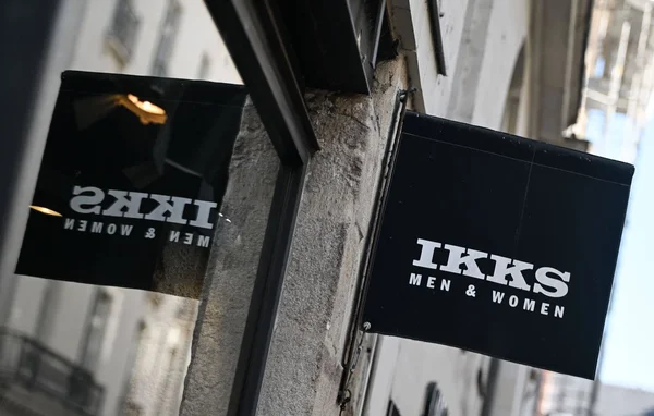 Enseigne de la marque IKKS sur un mur en pierre.