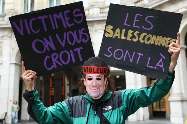 Un manifestant arbore un bandeau « VIOLEUR » et des pancartes de soutien aux victimes.