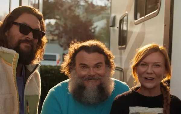 Jason Momoa en lunettes de soleil et gilet, Jack Black en barbe et pull bleu, Kirsten Dunst en pull noir devant un camping-car