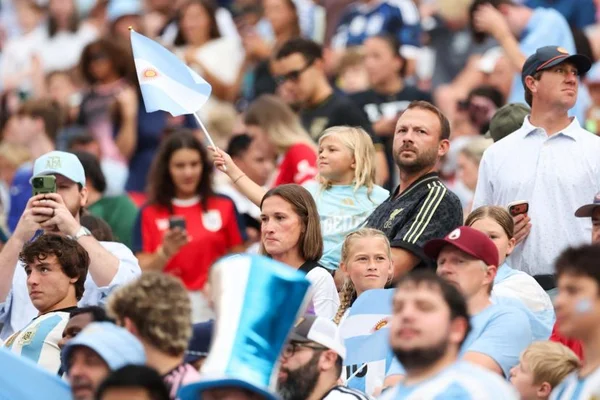 Une jeune supportrice argentine agitant un drapeau national dans un stade, entourée de fans.