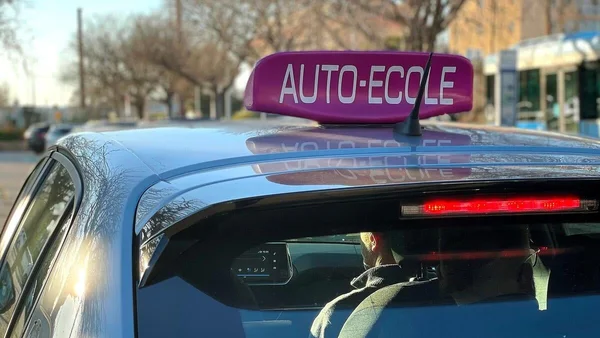 Panneau 'AUTO-ECOLE' sur le toit d'une voiture bleue, reflet sur la carrosserie.