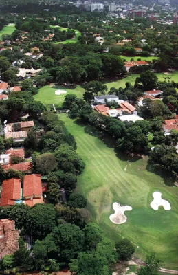 Terrain de golf du Caracas Country Club, entouré de maisons aux toits rouges et de la ville en arrière-plan.