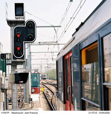 Un signal ferroviaire rouge et un train à l'arrêt illustrant une panne de signalisation.