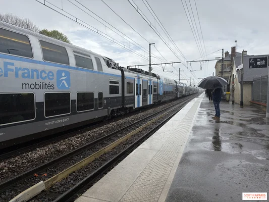 Train à l'arrêt en gare sous la pluie, illustrant les perturbations sur la ligne J.