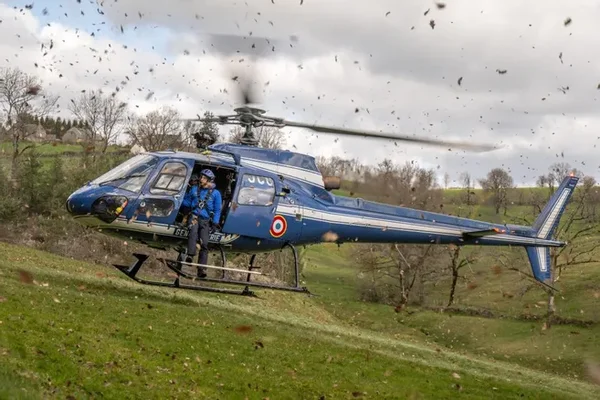 Hélicoptère de la Gendarmerie nationale en vol stationnaire au-dessus d'un terrain herbeux.