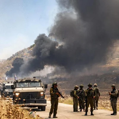 Soldats israéliens près d'un véhicule blindé alors qu'une fumée noire s'élève au loin.