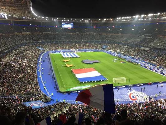 Le Stade de France en pleine cérémonie d'avant-match, avec des drapeaux tricolores.