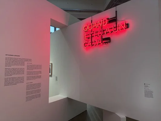Vue de l'exposition « Aux origines » : un néon rouge et un texte explicatif sur les discriminations.