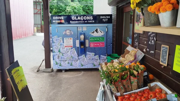 Distributeur de glaçons 'GLAÇONS' près d'un étal de fruits et légumes.