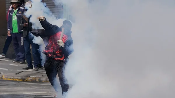 Un manifestant encagoulé lance un objet dans un nuage de gaz lacrymogène.