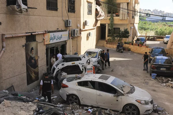 Des débris et des véhicules endommagés dans une rue de Beyrouth, avec un engin de chantier déblayant les gravats.