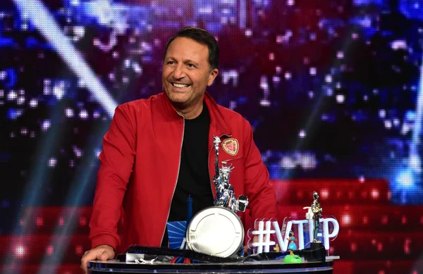 Arthur posant avec des trophées sur le plateau de District Z, devant un écran lumineux.