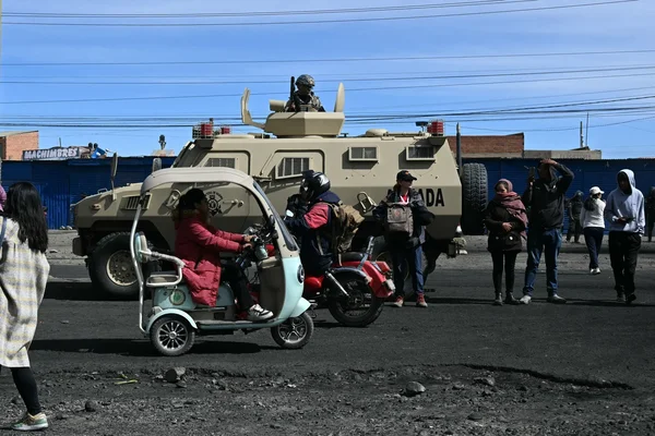 Véhicule blindé de l'armée bolivienne et soldat dans la tourelle, sur une route avec des civils et des tricycles.